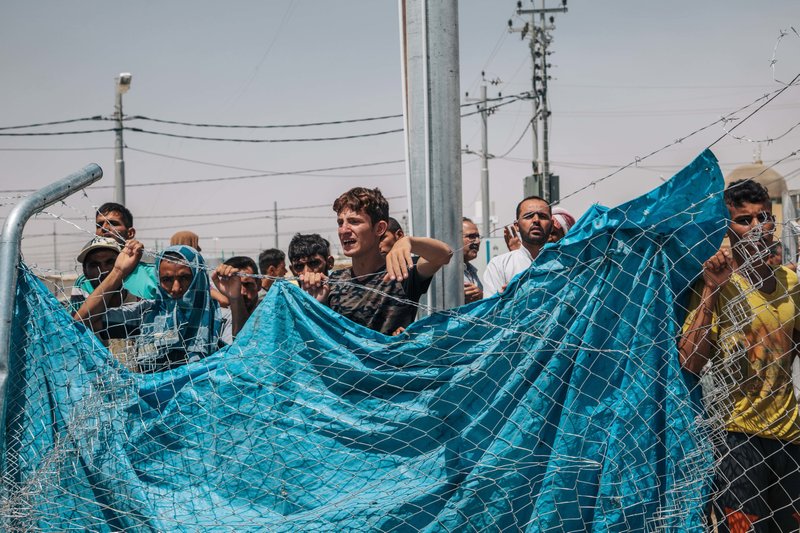 In this August 17, 2016 photo, men wait outside a fenced area at the Dibaga Camp for displaced people, where newcomers are interrogated before being allowed to stay, in Hajj Ali, northern Iraq.