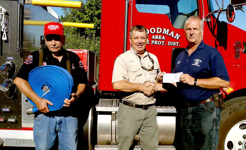 Rita Greene/McDonald County Press Left to right: Jimmie Morgan, president, Goodman Area Fire Protection Board, Terry Cook from the Neosho Missouri Department of Conservation office presenting Keith Estes, Goodman Fire Chief, with a $3,000 matching funds grant on Monday, Aug. 22. Morgan is holding one of the hoses which was purchased with the grant money.
