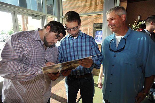 Actor Chris Severio (left), who plays Brandon Burlsworth in the movie "Greater, " autographs Tuesday, Aug. 23, 2016, a movie poster for Mark Marinoni, 16, of Fayetteville, who plays a role in the movie, as Marinoni's father, Paul Marinoni III, looks on during a red carpet event ahead of the premiere of the movie at the Malco Razorback Cinema 16 in Fayetteville. 