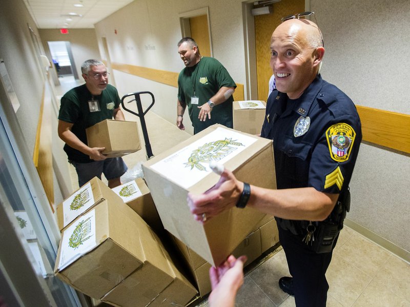 Sean Cocannouer (from left) and Nathan Porter, both with Northwest Arkansas Food Bank, and Rogers Police Sgt. Jose Dominguez help pass along boxes of meals Thursday at the Rogers Police Department. The food bank has partnered with the department to place the boxes, which each hold 10 meals, in police vehicles to distribute at their discretion while on calls. The program rolls out Sept. 1 to coincide with Hunger Action Month.