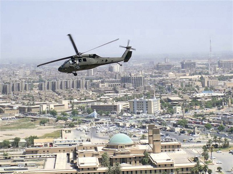 A Blackhawk helicopter flies over Baghdad during during the surge in Iraq. Army Chaplain Michael Tarvin took this picture from another Blackhawk as he flew over Baghdad on the way to a forward operating base. Tarvin kept a journal during the fighting and transformed the entries into a book of devotions: Light in the Midst of Darkness: Devotions From Combat. In the inset, Tavin waits in battle gear in front of a Blackhawk helicopter as it is refueled in a remote combat outpost. Army chaplains do not carry guns, Tarvin explained in his book. They are noncombatants focusing on their mission, ministering to soldiers. Rather, a chaplain’s assistant, with one assigned to each chaplain, carries the weapon and provides protection for the chaplain.