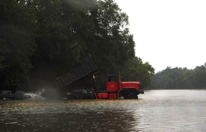A dump truck deposits a load of boulders in the Caddo River in the rain at Glenwood on Thursday to create a breakwater designed to relieve erosion on the river bank. The rain also dampened a father-daughter fishing trip.