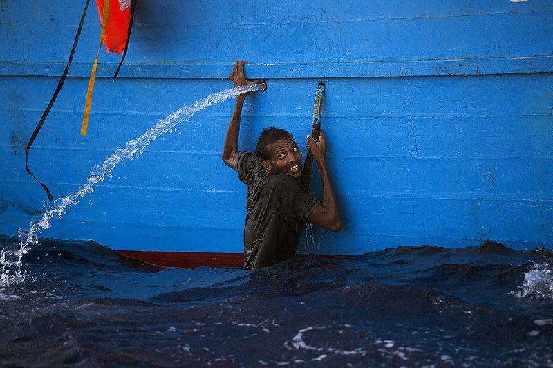 A man who jumped from a wooden boat crowded with migrants holds on to the side of the vessel Monday as he waits for rescue off the Libyan coast. The Italian navy and other groups reported rescuing thousands of migrants Monday.