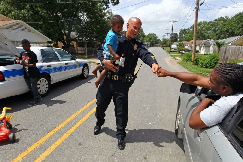 FILE — Police Officer Tommy Norman gets a fist bump from Roderick McClinton as he hands out water, snacks and toys to children at 16th and Sycamore streets while on patrol in July 2016 in downtown North Little Rock. (Arkansas Democrat-Gazette)