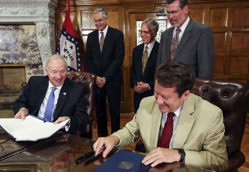 Gov. Asa Hutchinson (left) and Robert Califf, commissioner of the Food and Drug Administration, sign a memorandum of understanding extending a federal-state partnership regarding the FDA’s National Center for Toxicological Research in Jefferson.  