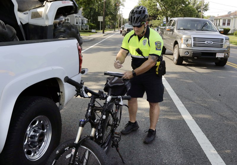 In this Wednesday, July 20, 2016 photo, police officer Matthew Monteiro writes a citation for a motorist who was texting while driving, after pulling the vehicle over while patrolling on his bicycle in West Bridgewater, Mass.