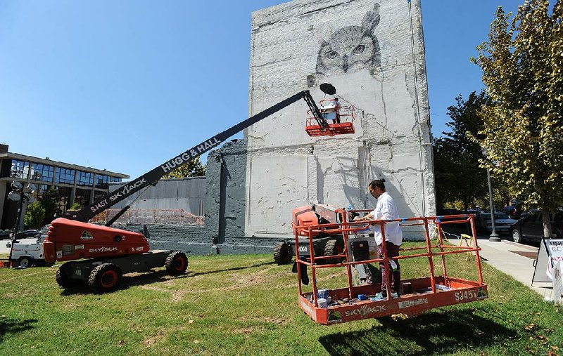 Artist Alexis Diaz (top) works from a painter’s lift Saturday as artist and assistant Tenchi prepares to join him as they create a mural at College Avenue and East Center Street in Fayetteville.