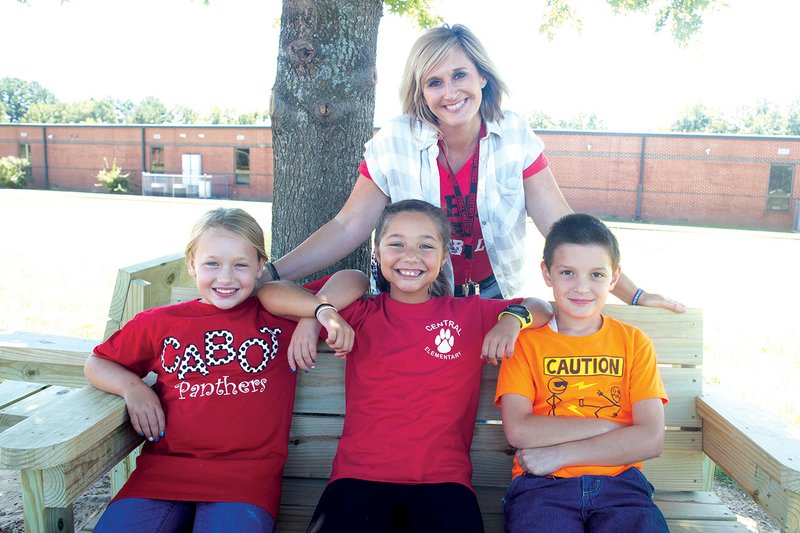 Central Elementary School Principal Bethany Hill stands behind Keira Tabor, from left, Joslyn Wooten and Aidan Diaz as the kids sit on one of the new Buddy Benches in the school’s playground.