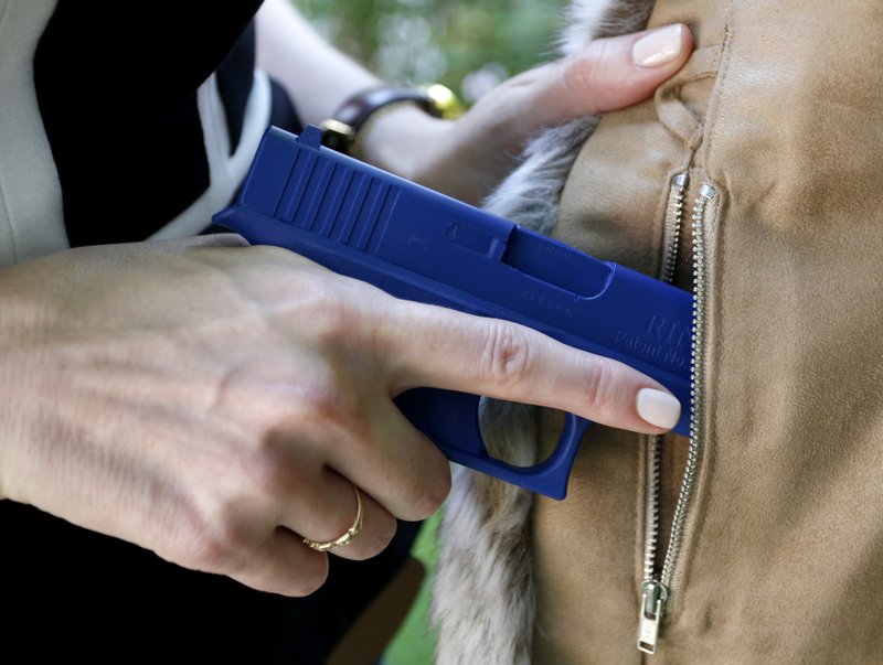 In this Aug. 29, 2016 photo, Marilyn Smolenski uses a mock gun to demonstrate how to pull a handgun out of the concealed carry clothing she designs at her home in Park Ridge, Ill. Interest in clothing that allow women to carry a firearm concealed is rising. Pioneers in the industry say they allow women to avoid looking frumpy and still carry a firearm safely and effectively. (AP Photo/Tae-Gyun Kim)