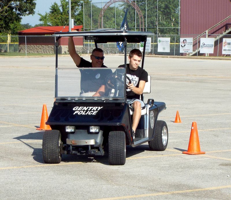 Photo by Randy Moll Braxton Gunneman, a senior at Gentry High School (right), accompanied by Gentry Police Chief Keith Smith, drives a police department golf cart around a course marked with cones in preparation to repeat the course wearing goggles which simulate impaired vision from being under the influence of alcohol or drugs. Students participated Sept. 7 in the Fatal Vision driving exercise to illustrate the danger of drinking and driving.