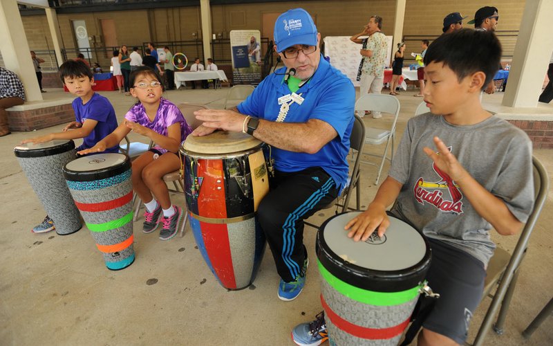 Al “Papa Rap” Lopez (center) leads Lee Gottlieb (right), 12, of Bentonville in a lesson on the bongos Saturday during Welcome Week NWA 2016 at the Shiloh Square in Springdale. The annual event is presented by Engage NWA to get minorities engaged and involved with their cities and communities by connecting them with area agencies and organizations and providing exposure to other cultures.