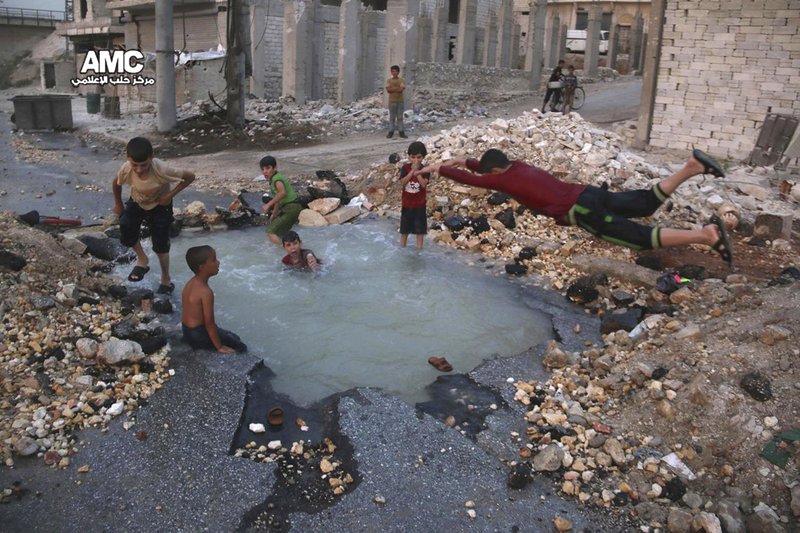 This Aug. 31, 2016 file photo, provided by the Syrian anti-government activist group Aleppo Media Center (AMC), shows Syrian boys dive into a hole filled with water that was caused by a missile attack in the rebel-held neighborhood of Sheikh Saeed in Aleppo province, Syria. 