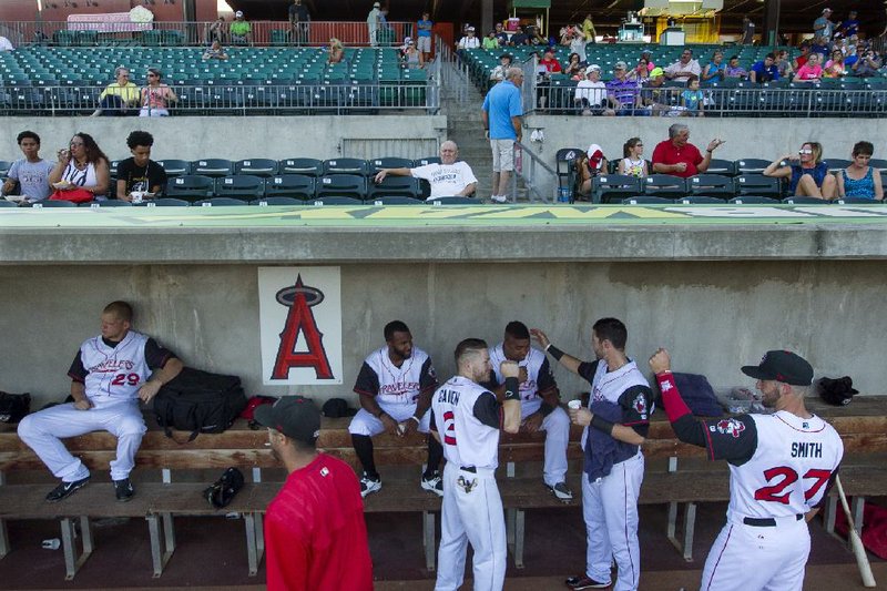 Members of the Arkansas Travelers visit with each other prior to the start of a 2015 game against the Northwest Arkansas Naturals. The Los Angeles Angels logo in the dugout will change to a Seattle Mariners logo after the Travelers announced a new affiliation agreement Tuesday with the American League West team.
