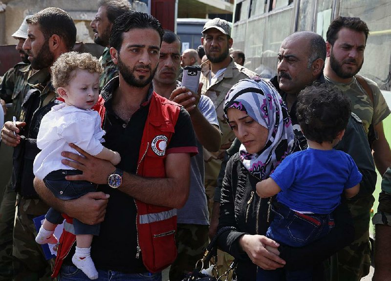 Syrian Arab Red Crescent workers assist fi ghters’ families as they leave Thursday from Al-Waer, the last rebel-held neighborhood in Homs.