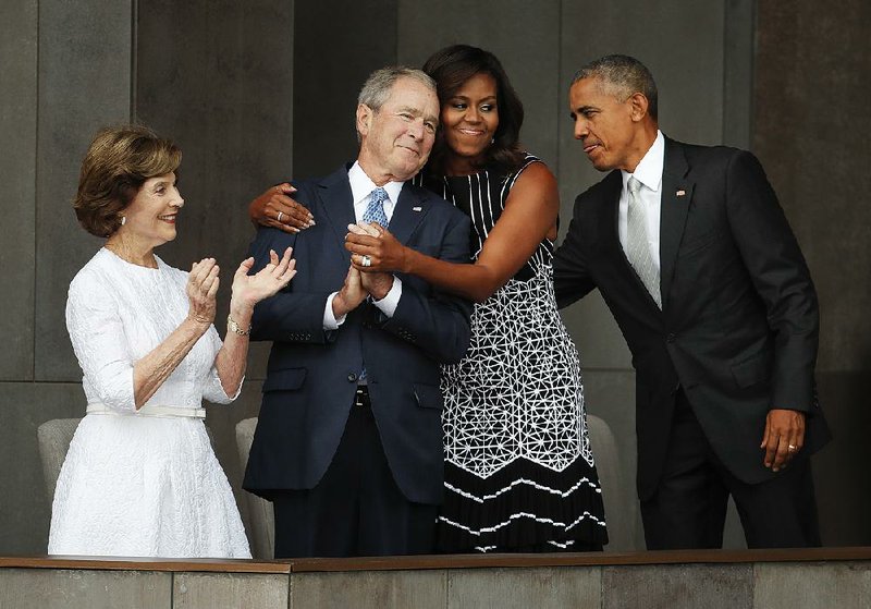 Former President George W. Bush gets a hug from fi rst lady Michelle Obama as they take the stage, along with former first lady Laura Bush and President Barack Obama, for Saturday’s ceremony.