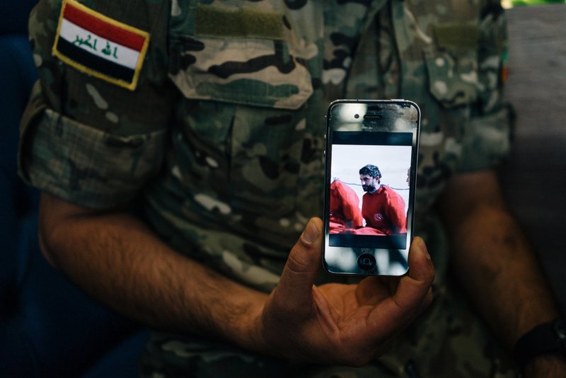 In this Aug. 10, 2016 photo, Iraqi Army Cpl. Saif holds a phone displaying a screenshot from a video released by the Islamic State group that shows his brother, in Irbil, Iraq.