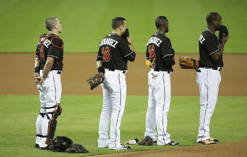 Third baseman Martin Prado (from left), shortstop Adeiny Hechavarria and left fi elder Marcell Ozuna look at a video during a pregame ceremony honoring pitcher Jose Fernandez before Miam’s game game against the New York Mets on Monday. The Marlins players all wore No. 16 in remembrance of Fernandez, who died in a boating accident Sunday.