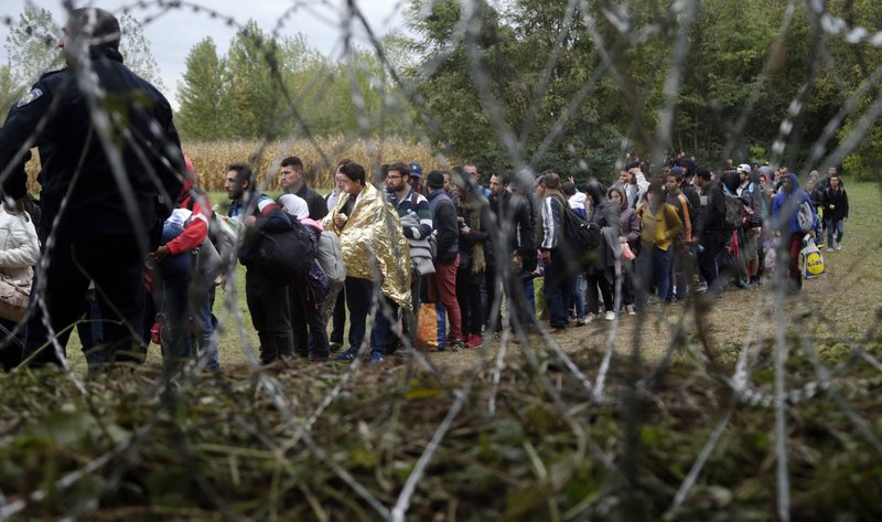 In this Saturday, Sept. 26, 2015 file photo, a group of migrants, seen through razor wire, crosses a border from Croatia near the village of Zakany, Hungary. 