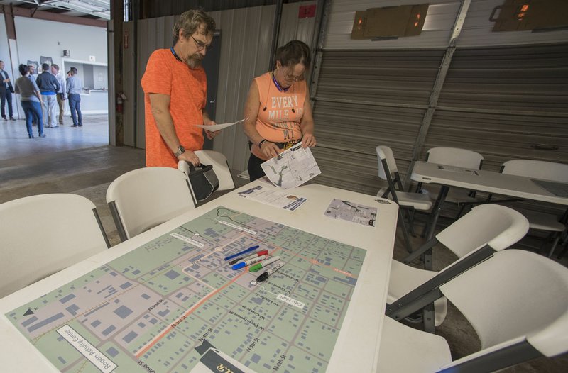 Brian and Danielle Leitch of Rogers look at maps Thursday before a public meeting at the downtown Rogers Farmers market for the BikeNWA project. The project, which is taking place in multiple cities, will build the region’s first protected bike lanes. The first step in Rogers is a demonstration project connecting the Railyard Bike Park to the Rogers Activity Center.