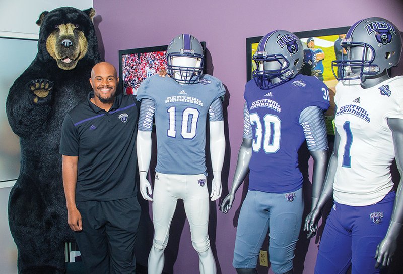 Larry Hart, a new assistant football coach at the University of Central Arkansas, stands by the school’s bear mascot, as well as some of the uniforms for the team. Hart played two seasons for the Bears before embarking on a career in professional football. He was hired as the Bears’ defensive line coach Aug. 1.
