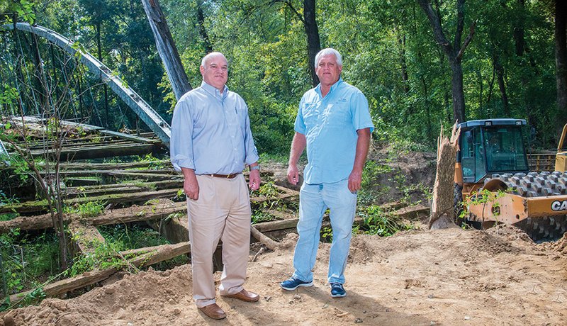 Jack Bell, left, chief of staff for the city of Conway, and Steve Ibbotson, director of the Conway Parks and Recreation Department, stand at the foot of the 1874 Springfield Des-Arc Bridge, which will be moved to Beaverfork Lake in Conway. Work is underway to clear the road and make a gravel pad for a crane to sit on as it lifts the bridge — scheduled for the first of November — so it can be restored. The bridge spans Cadron Creek at the Faulkner-Conway county line.