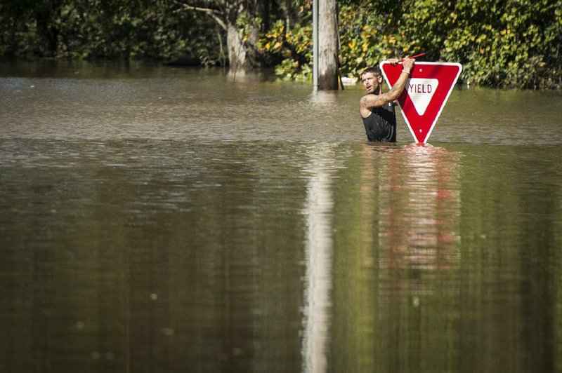 A man holds on to a yield sign after trying to swim out to help a stranded truck driver at an intersection in Hope Mills, N.C., on  Sunday. Both were rescued.