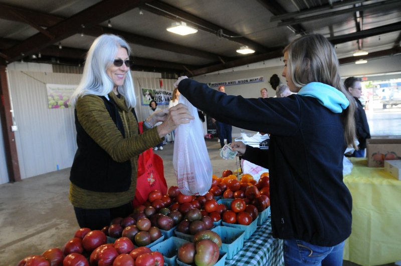 Wanetta Morrill of Rogers (left) buys tomatoes Saturday from Averi Johnson at the McGarrah Farms table at the Downtown Rogers Farmers Market. The farm-to-school program in Fayetteville interested Dennis McGarrah, and he started looking into it, he said. He turned in bids and won contracts for tomatoes, strawberries and bell peppers.