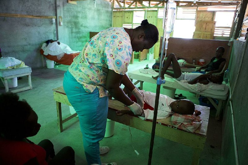 Nurse Mardi Rose Guerline adjusts the IV on 9-year-old Franzy Noel as his mother Geraldine Pierre looks on Tuesday in a cholera ward in Les Cayes, Haiti. 