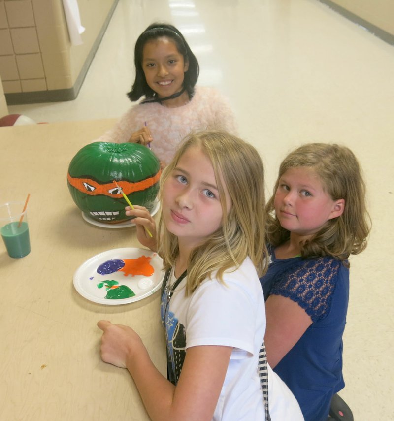 Photo by Susan Holland These young artists in Mr. Briggs&#8217; fourth grade class at Gravette Upper Elementary School were putting the finishing touches on their class&#8217;s double-sided Teenage Mutant Ninja Turtle pumpkin last Friday. Faith Croxdale and Perri Miller (in the foreground) were painting the front of the pumpkin, and Emily Lopez (in back) painted the reverse side. Their artwork is on display at the Gravette Harps store this week, along with other creations from GUE and Glenn Duffy Elementary.