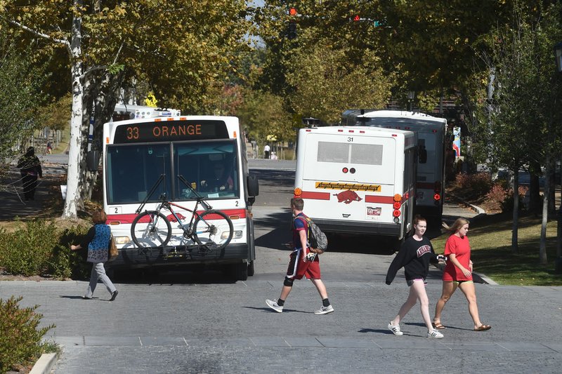 University of Arkansas students cross Garland Avenue on Tuesday as buses make their way to the bus stops at the University of Arkansas campus in Fayetteville.