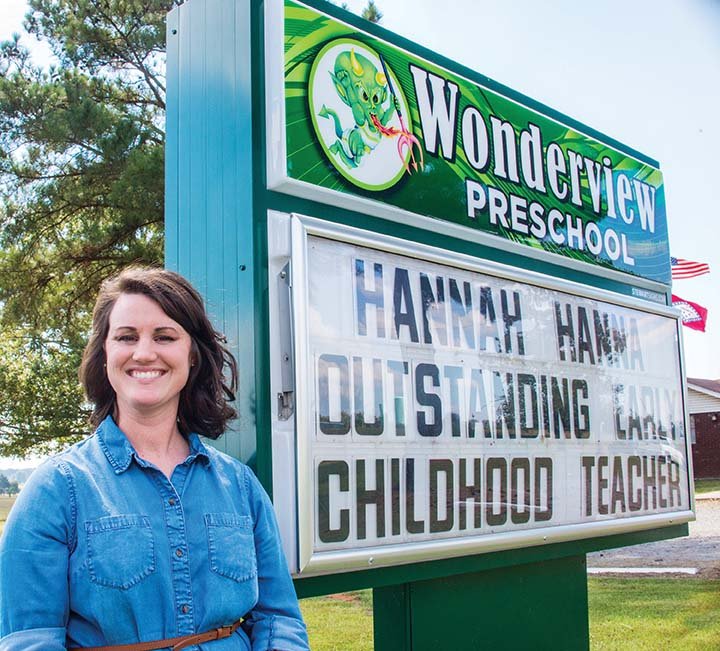 Hannah Hanna of Hector, lead teacher and director of Wonderview Preschool in Hattieville, stands by the sign that congratulates her on being named Outstanding Early Childhood Professional of the Year for 2016. Hanna, 26, and her husband, Donnie, raised chickens for a corporation before she went back to college to become a teacher.