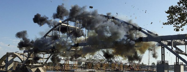 Explosive charges go off across the Broadway Bridge’s steel arch Tuesday morning. The charges were supposed to drop the bridge into the Arkansas River, but it held on, barely teetering.