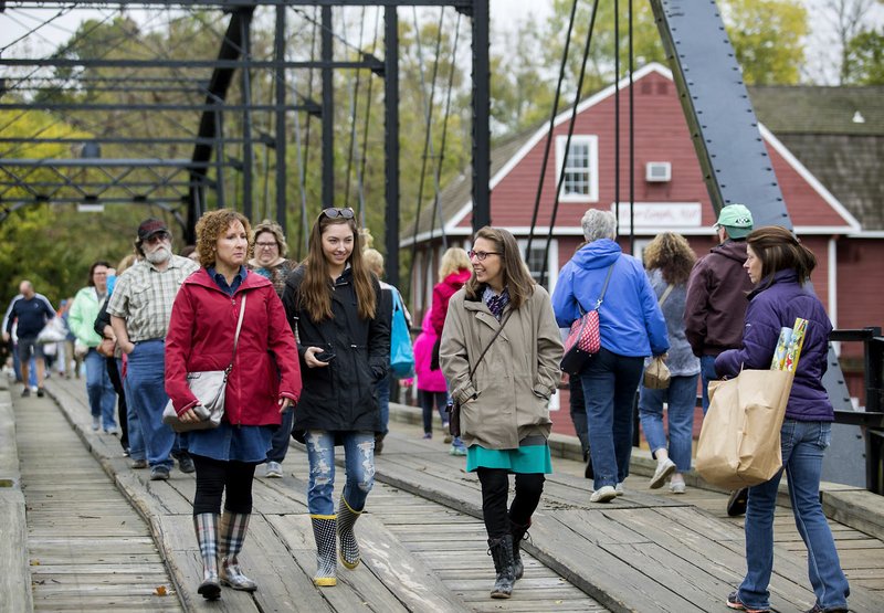 Lori Smith (from left), Kariah Brust, both of Tulsa, Okla., and Sandy Brust of Bentonville cross the bridge Thursday during the annual fall War Eagle Craft Fair at the War Eagle Mill.