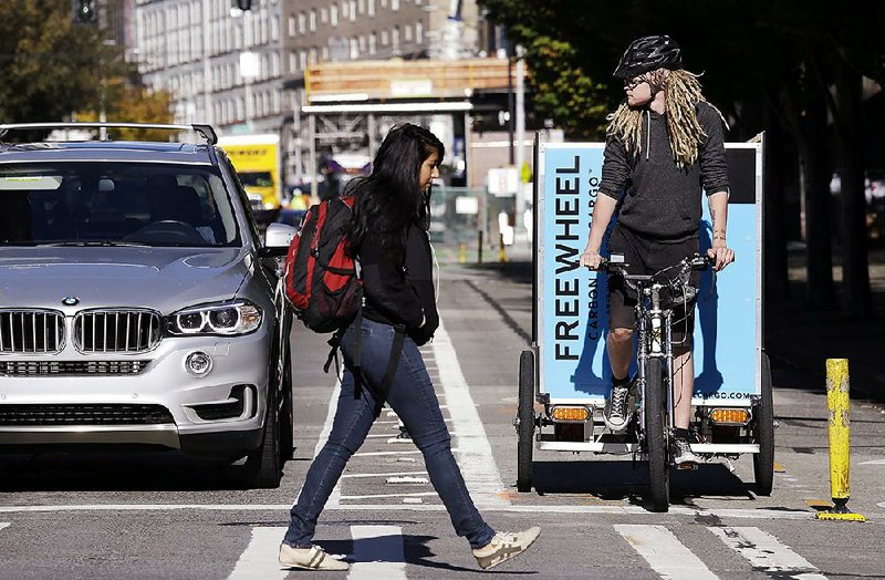 Cargo bike delivery driver Jesse Erickson looks out over traffic as a pedestrian passes in front of his bicycle lane on a downtown street Wednesday in Seattle.