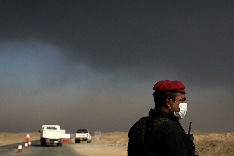 An Iraqi special forces soldier wears a mask Saturday at a checkpoint south of Mosul as the sky fills with smoke and gas fumes from oil and sulfur-plant fires set by Islamic State militants. The noxious air is causing breathing difficulties for civilians and Iraqi forces advancing on the city. 