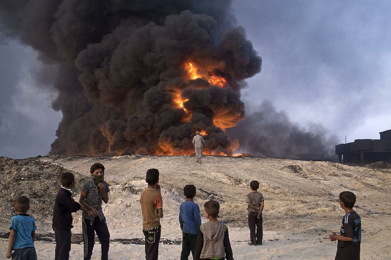 People watch a burning oil well in Qayyarah, about 31 miles south of Mosul, Iraq, on Sunday. Islamic State fighters torched a sulfur plant south of Mosul, sending a cloud of toxic fumes into the air that mingled with smoke from oil wells the militants had set on fire to create a smoke screen.