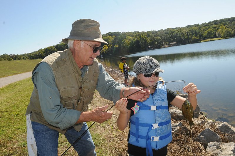 Lloyd Okeson with the Bella Vista Fly Tyers helps Eve Reagan catch a sunfish at Lake Windsor. Members of the fishing group helped students from R.E. Baker Elementary in Bentonville with their fishing during a nature education day at the lake.