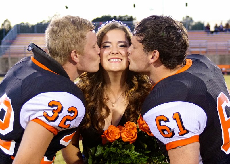 Photo by Randy Moll Bret Callahan and Cody Sullins give a ceremonial kiss to Alex Krewson after she was crowned homecoming queen at Gravette High School homecoming ceremonies in Lion Stadium on Friday night (Oct. 21, 2016).