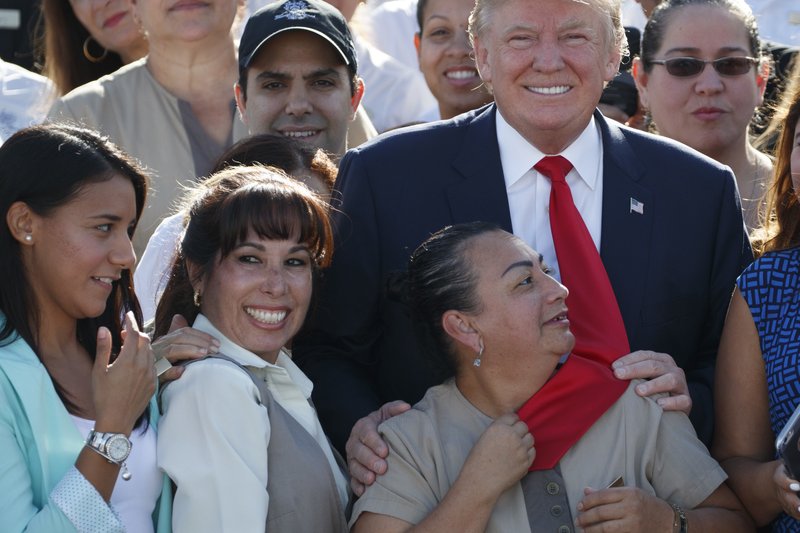 An employee of Republican presidential candidate Donald Trump grabs his tie as they pose for photographs during an event at Trump National Doral, Tuesday, Oct. 25, 2016, in Miami. (AP Photo/ Evan Vucci)
