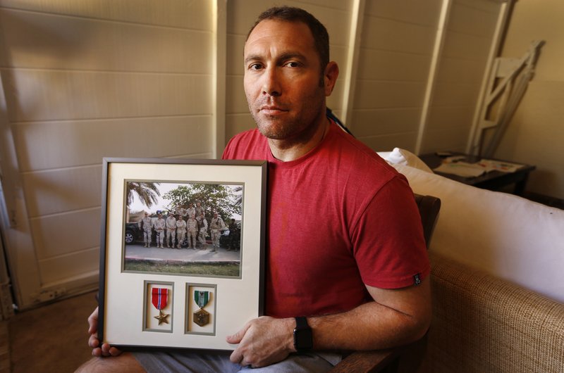 In this Friday, Oct. 21, 2016 file photo, Robert D'Andrea, a retired Army major and Iraq war veteran, holds a frame with a photo of his team on his first deployment to Iraq in his home in Los Angeles. Nearly 10,000 California National Guard soldiers have been ordered to repay huge enlistment bonuses a decade after signing up to serve in Iraq and Afghanistan, the Los Angeles Times reported Saturday.