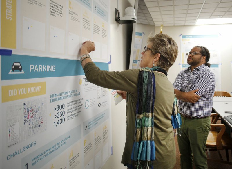 Kevin Lucas (right) with Nelson/Nygaard Consulting Associates watches Tuesday as Susan Norton, Fayetteville communication and marketing director, places an input sticker on a feedback display at City Hall in Fayetteville.