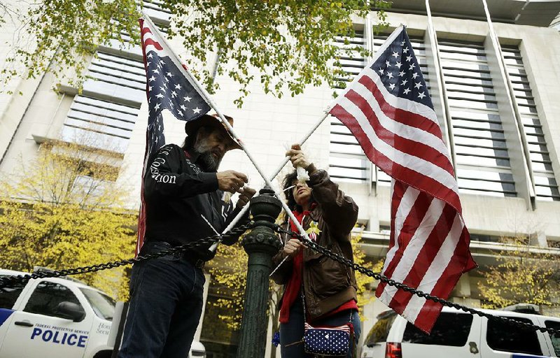 David Brugger and Maureen Valdez attach American flags to a rail post Tuesday outside the federal courthouse in Portland, Ore., where defendants in a standoff last winter are on trial.