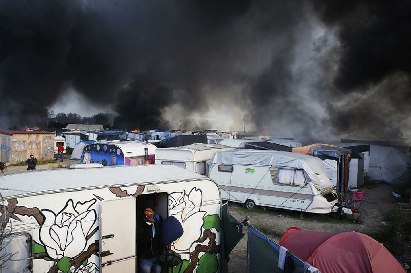 A man carrying his belongings flees a trailer Wednesday as smoke rises from tents set aflame in the makeshift migrant camp known as “the jungle” near Calais in northern France.