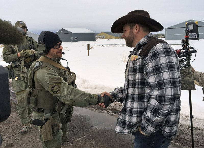 FILE - In this Jan. 22, 2016, file photo, Ammon Bundy, right, shakes hand with a federal agent guarding the gate at the Burns Municipal Airport in Burns, Ore. 