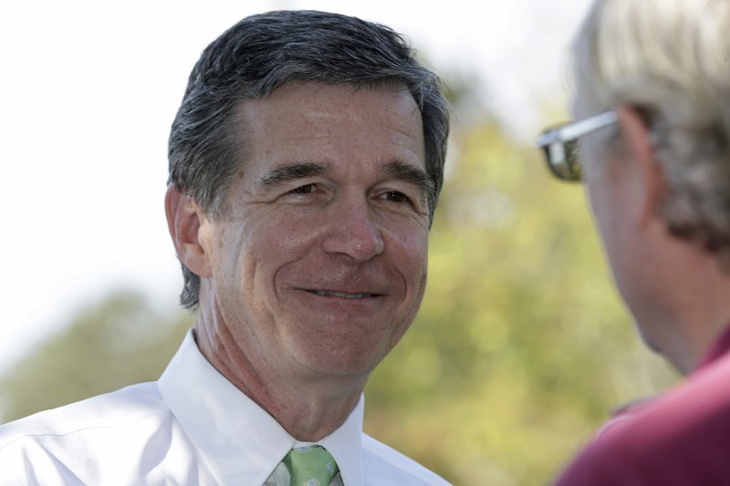 In this photo taken Thursday, Oct. 20, 2016 Democratic gubernatorial candidate Attorney General Roy Cooper mingles with voters at the polls during early voting in Raleigh, N.C. 