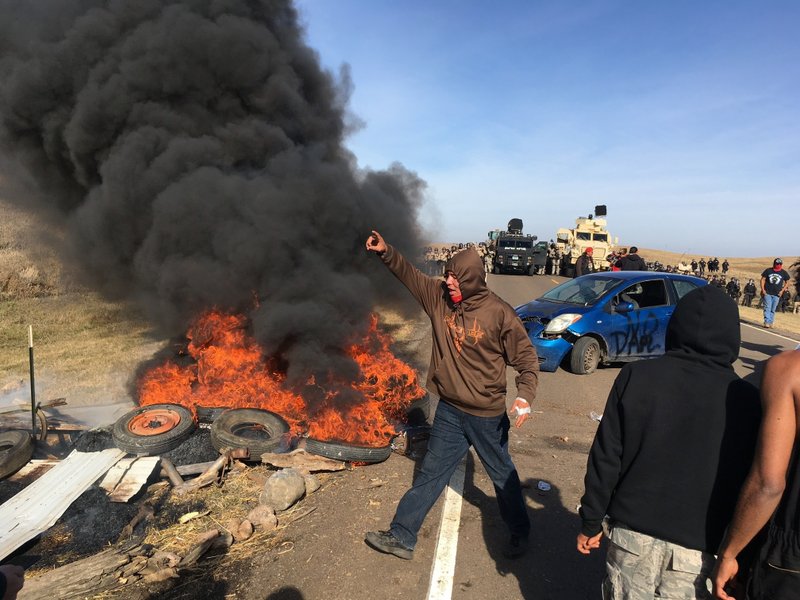 Demonstrators stand next to burning tires as armed soldiers and law enforcement officers assemble on Thursday, Oct. 27, 2016, to force Dakota Access pipeline protesters off private land where they had camped to block construction. The pipeline is to carry oil from western North Dakota through South Dakota and Iowa to an existing pipeline in Patoka, Ill. 