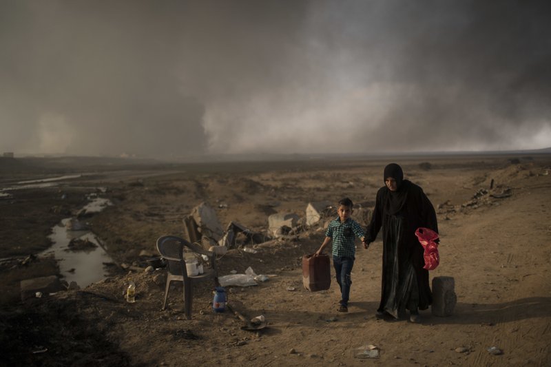Displaced people walk past a checkpoint near Qayara, south of Mosul, Iraq, Sunday, Nov. 6, 2016. 
