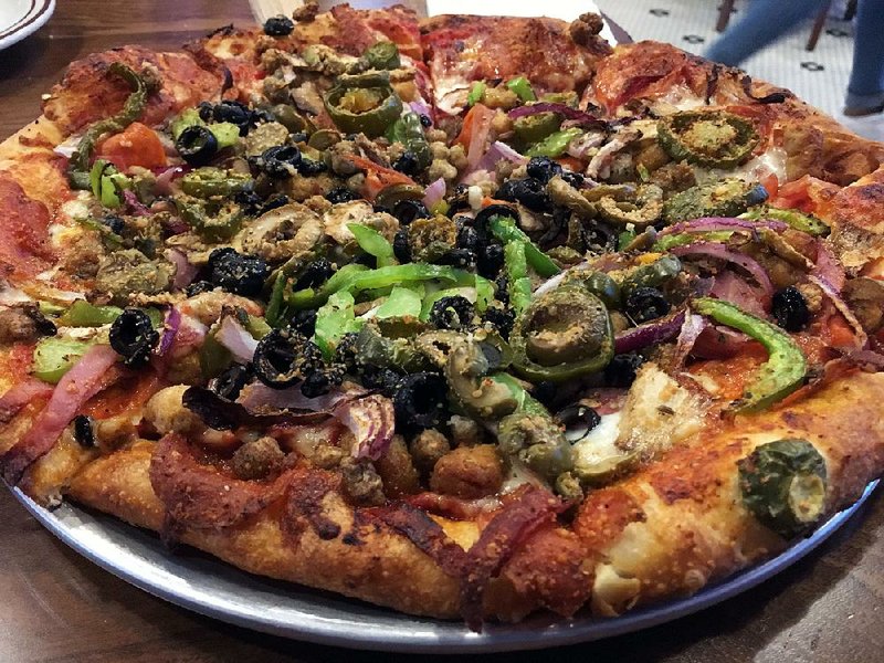 A build-your pizza with Italian sausage and mushrooms rests on the bar, where full service is available, at Hideaway Pizza in North Little Rock. 