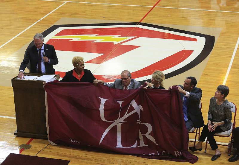 UALR Chancellor Andrew Rogerson (left) speaks Wednesday as Jacksonville High School Principal LaGail Biggs (second from left) and members of the Wilson family hold a UALR flag during a ceremony to announce the Jacksonville Promise program. Family members (from left) are Larry Wilson, wife Wendy Wilson, son Patrick Wilson and sister Kathy Roberts.