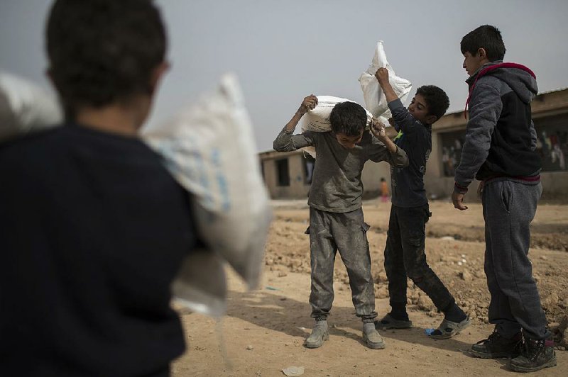 Iraqi boys displaced by fighting in Mosul carry food distributed at a refugee camp Thursday in Hassan Sham, east of the city.
